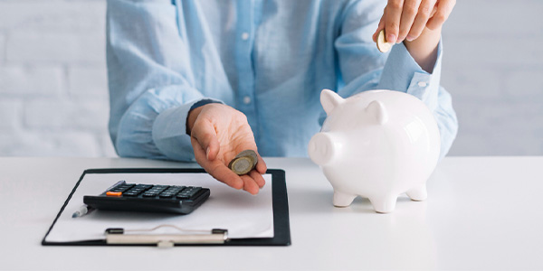 Man putting coins into white piggy bank, next to a calculator